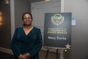 Mary Davila stands proudly next to a sign celebrating her historic achievement as Peter Pan Bus Lines’ first female 2 Million Mile Safe Driver at the 2025 STAR Awards.