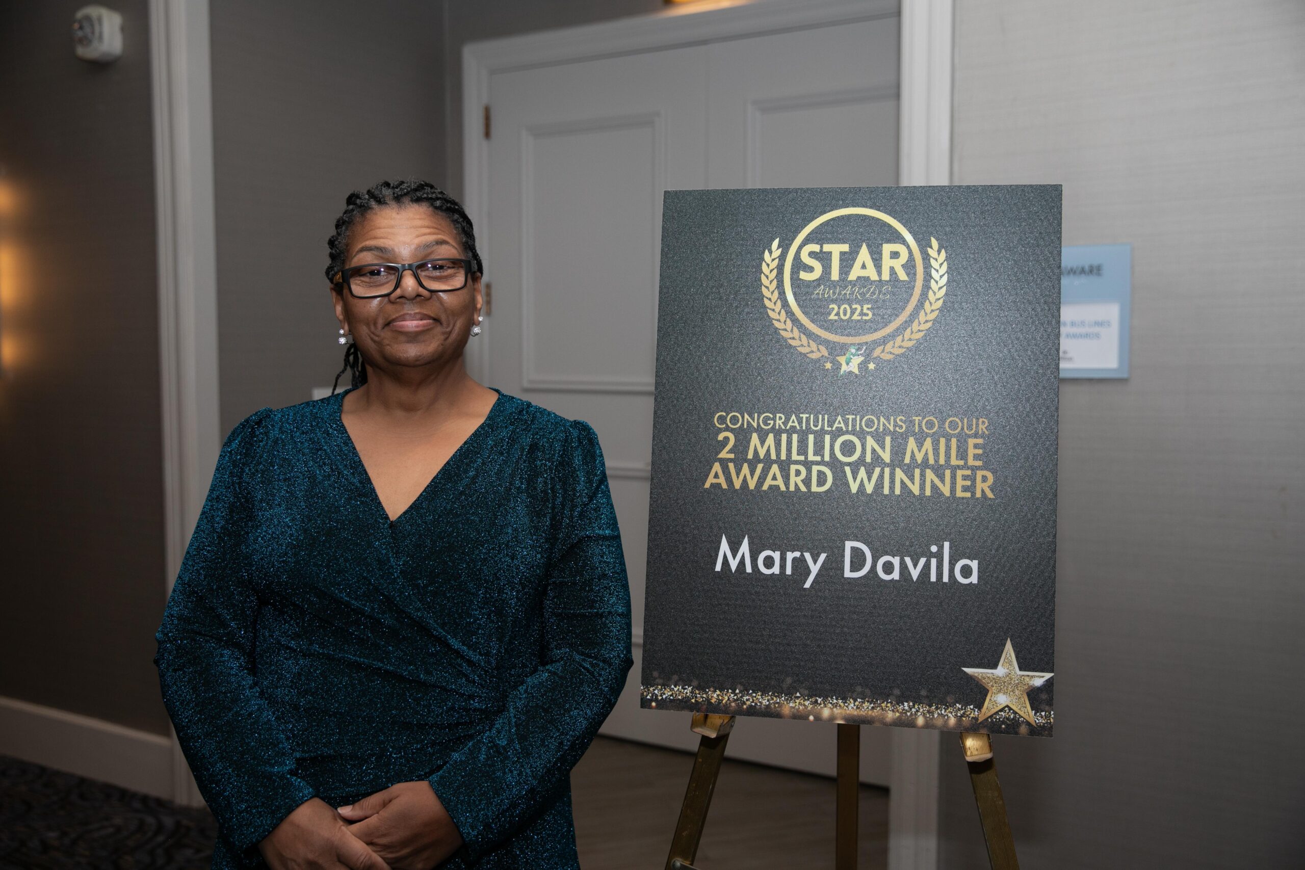 Mary Davila stands proudly next to a sign celebrating her historic achievement as Peter Pan Bus Lines’ first female 2 Million Mile Safe Driver at the 2025 STAR Awards.