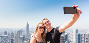 Couple taking a selfie at Top of the Rock in New York City, enjoying stunning skyline views. Arrive stress-free with Peter Pan Bus Lines for a romantic Valentine’s Day experience