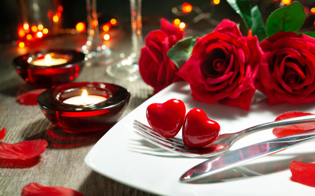 Romantic Valentine's Day dinner setting with red roses, candles, and a love-themed place setting.